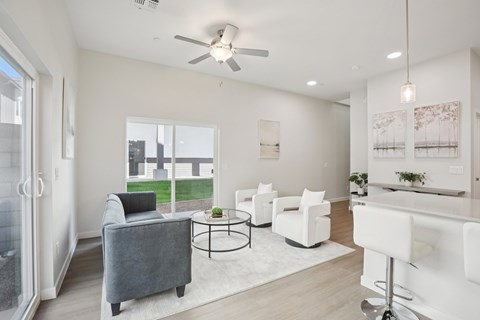 A living room with a grey sofa, white chairs, and a ceiling fan.