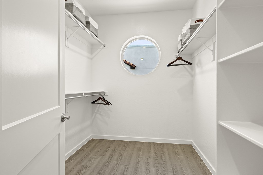 a walk in closet with a round window and white walls and wooden floors