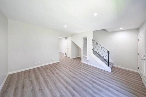 a living room with white walls and a white staircase and wood flooring
