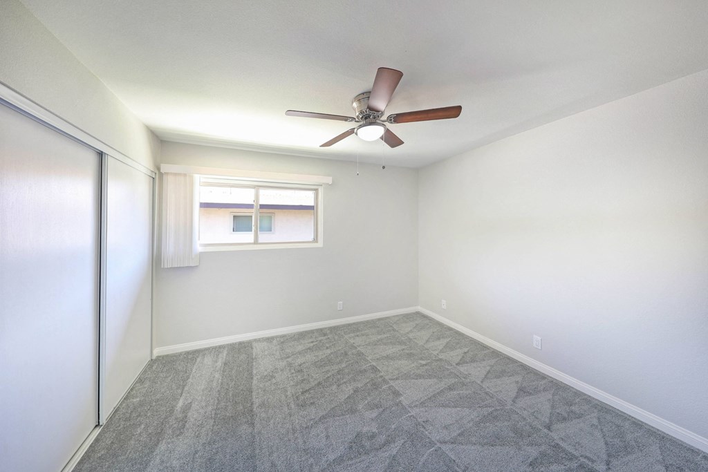 an empty bedroom with a ceiling fan and closet