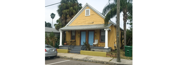 A yellow house with a blue door and a car parked in front.