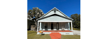 A small white house with a porch and a sign that says "NOW LEASING".