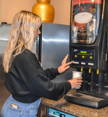 a woman putting a cup into a coffee vending machine at Campus Park, Duluth
