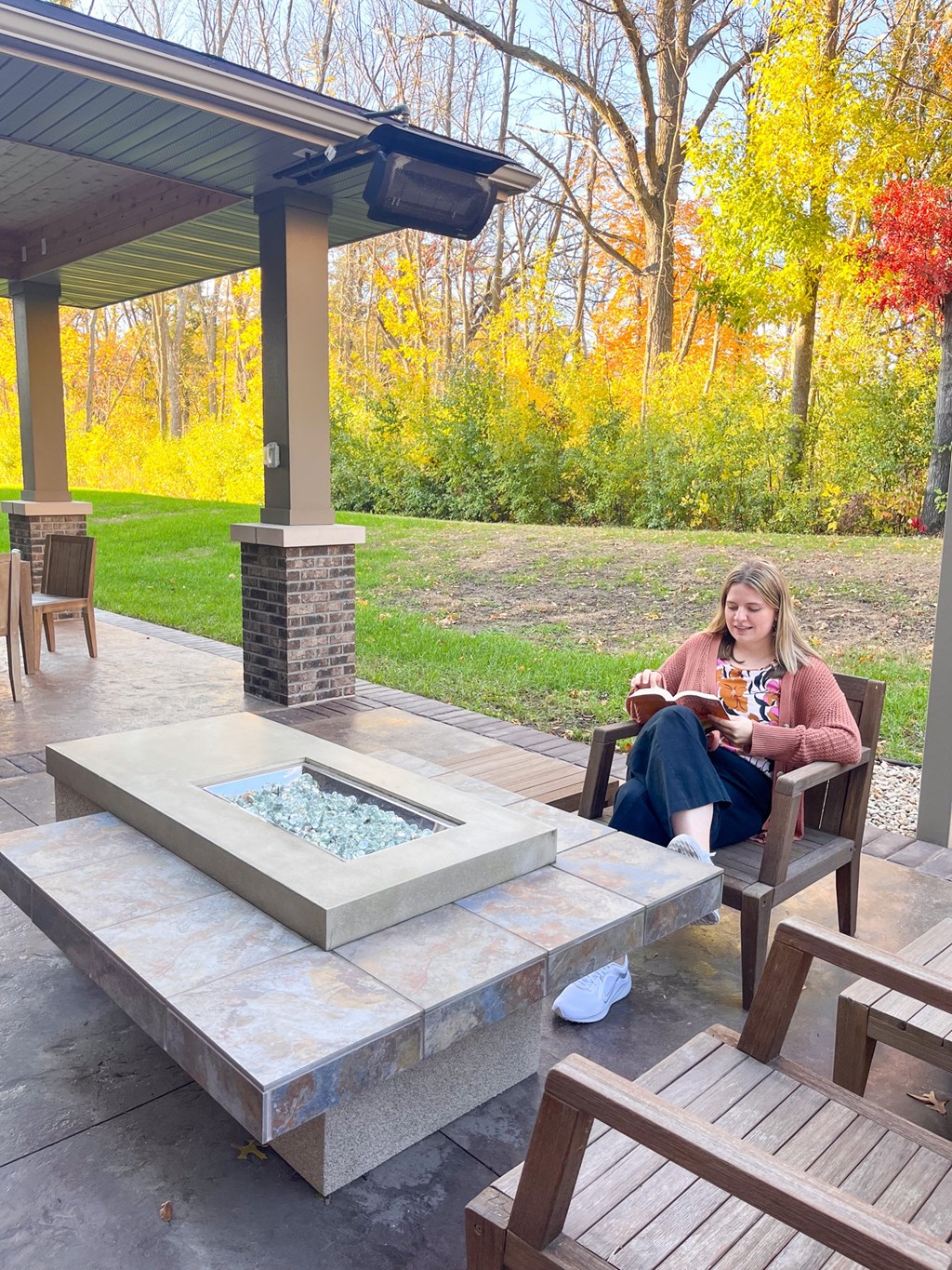 A woman is sitting on a chair on a patio with a fire pit in front of her.