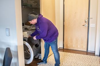 a man is putting laundry into a washing machine in a closet at Bluestone Lofts, Duluth, MN