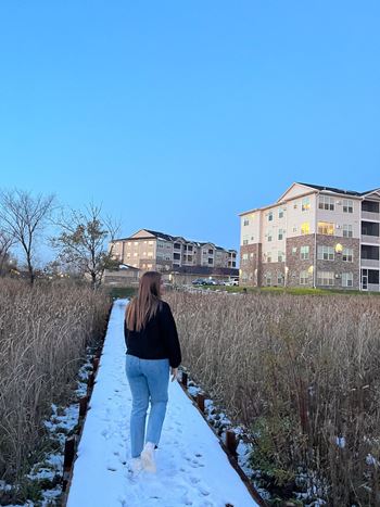 A person is walking on a snow-covered path with buildings in the background.