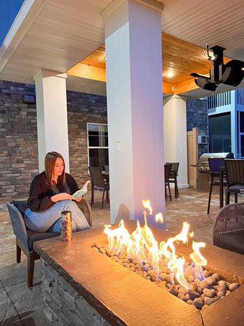 A woman is sitting by a fireplace on a patio.