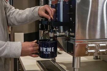 a person making a cup of coffee in a coffee machine at Bluestone Lofts, Duluth, MN, 55803
