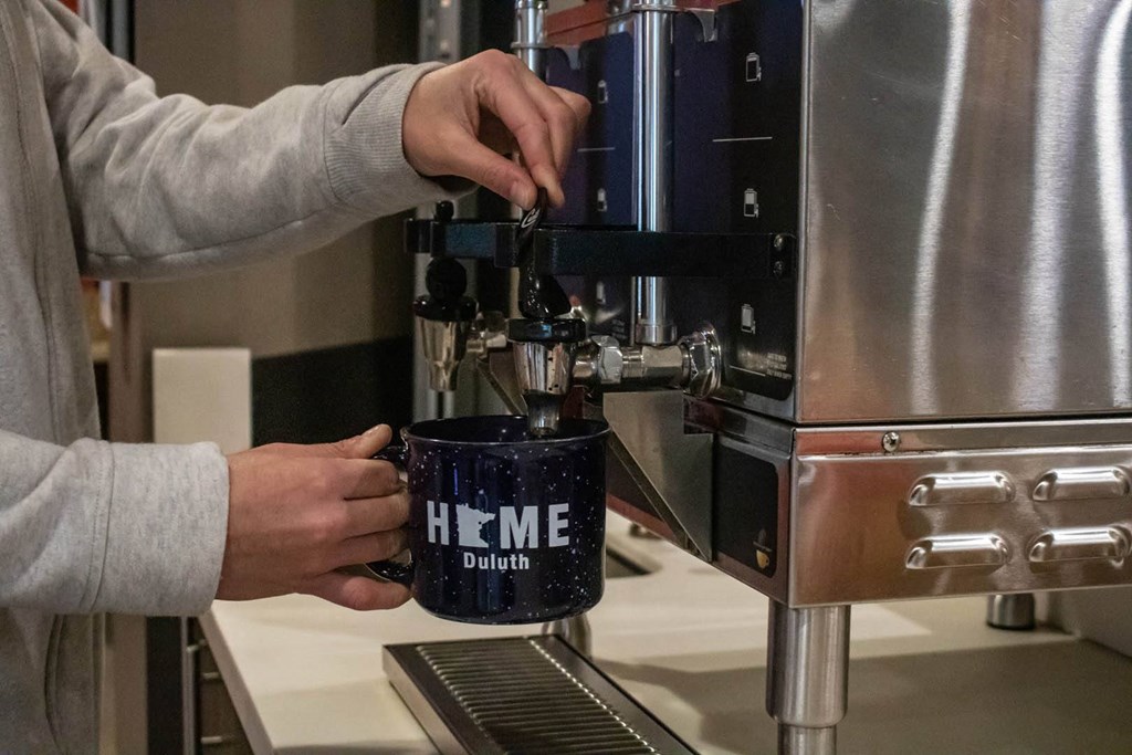 a person making a cup of coffee in a coffee machine at Bluestone Lofts, Minnesota, 55803
