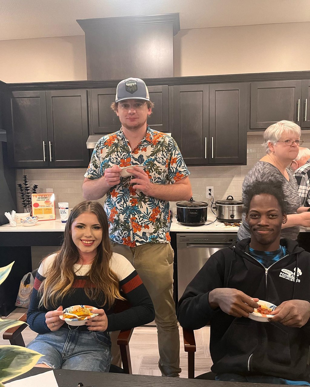 a group of people standing in a kitchen holding plates of food  at Timber Ridge, Forest Lake, MN