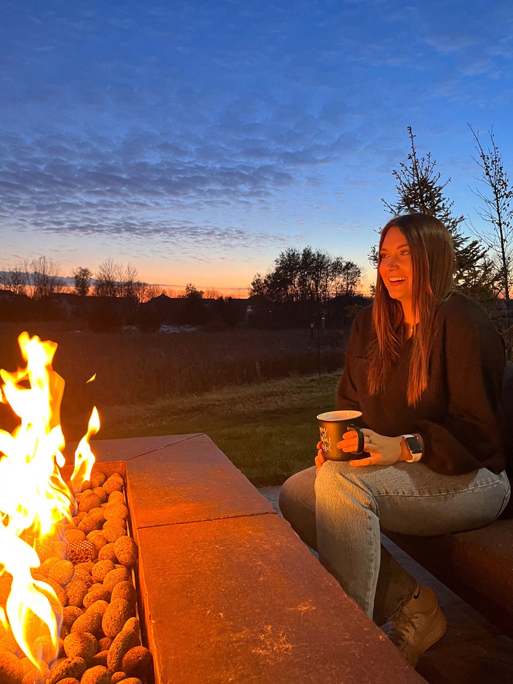 a woman sitting next to a fire with a cup of coffee  at Timber Ridge, Forest Lake, 55025