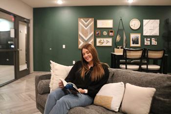A woman is sitting on a grey couch reading a book.