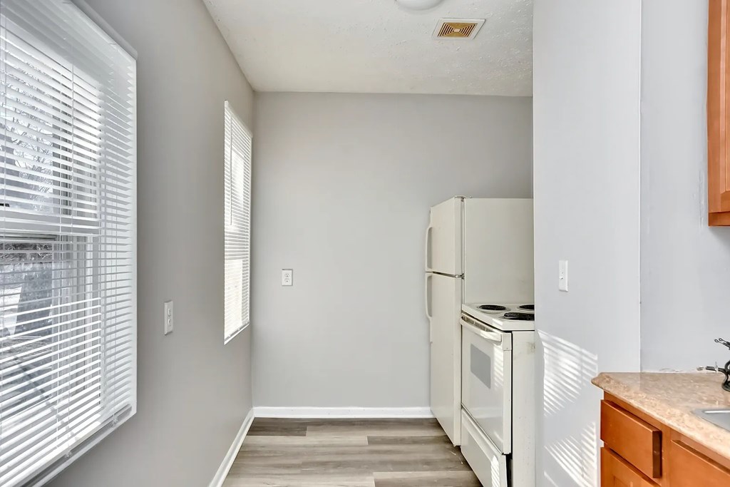 A kitchen with a white fridge and a window with blinds.