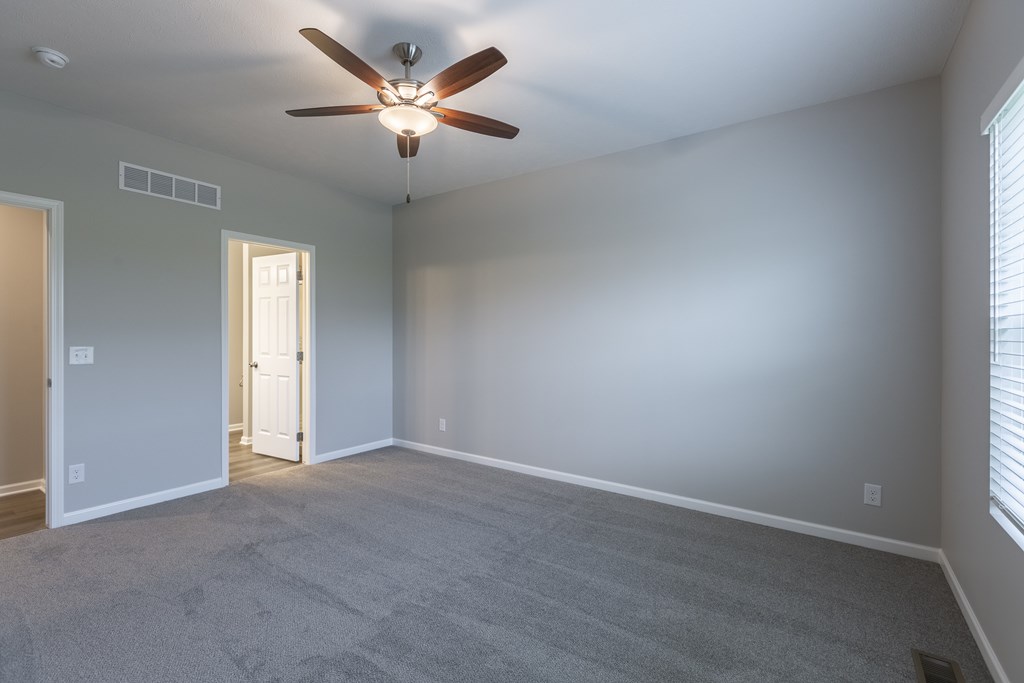 A room with a ceiling fan and carpeted floor.