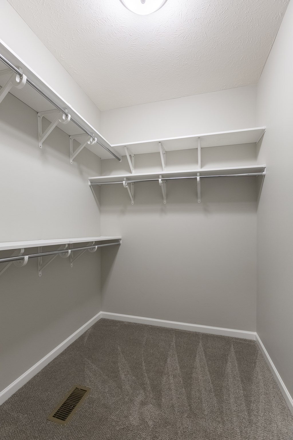 A white closet with a carpeted floor and a vent in the floor.