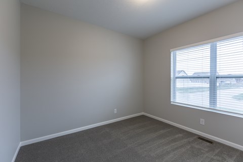 A room with a carpeted floor and a window with blinds.