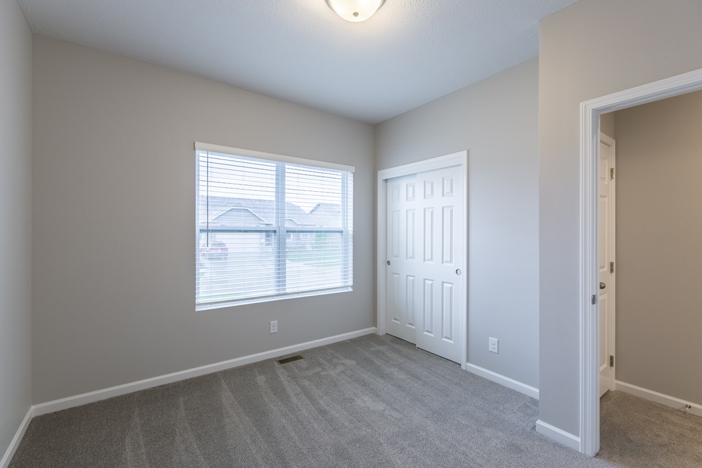 A room with a carpeted floor, a window with blinds, and a white door.