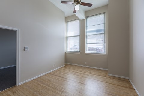 A room with a ceiling fan and two windows.