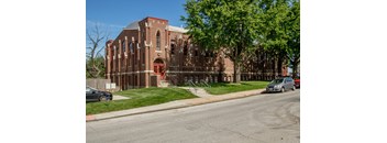 Exterior view of a multi story brick apartment building with landscaped lawn and sidewalk at 3 Point Lofts.