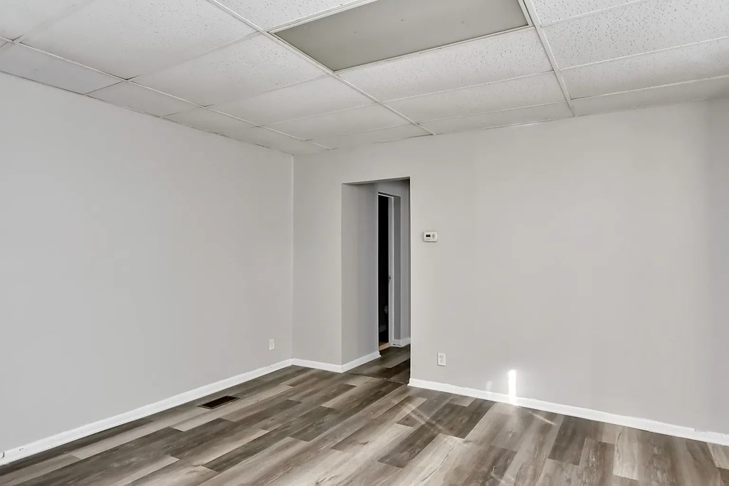 A room with a wooden floor and a white ceiling with a door on the right side.