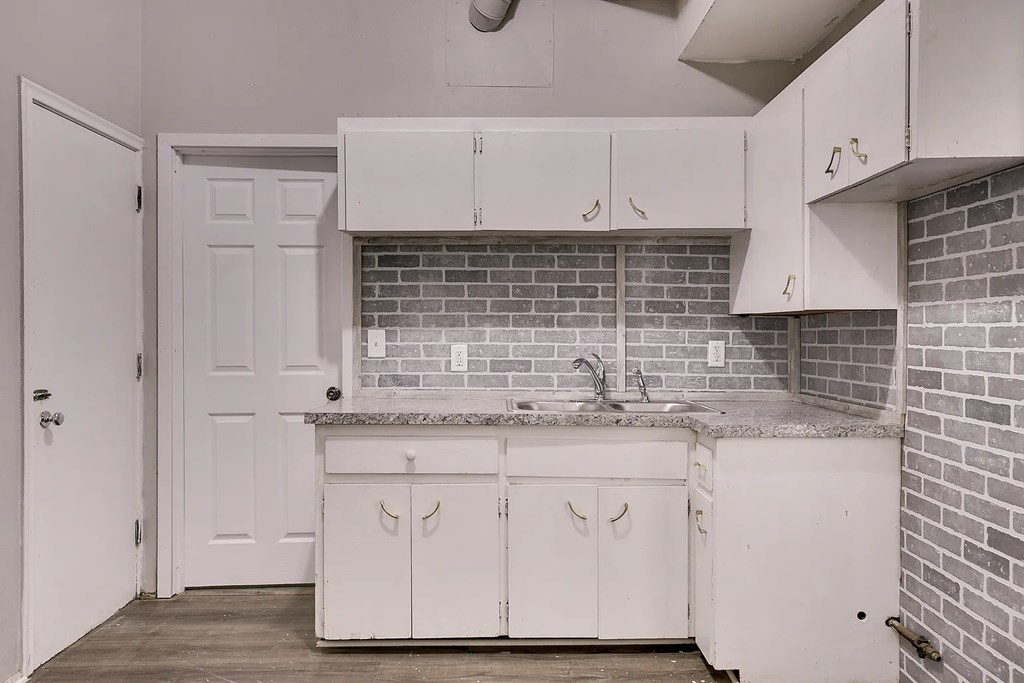 A kitchen with white cabinets and a brick backsplash.