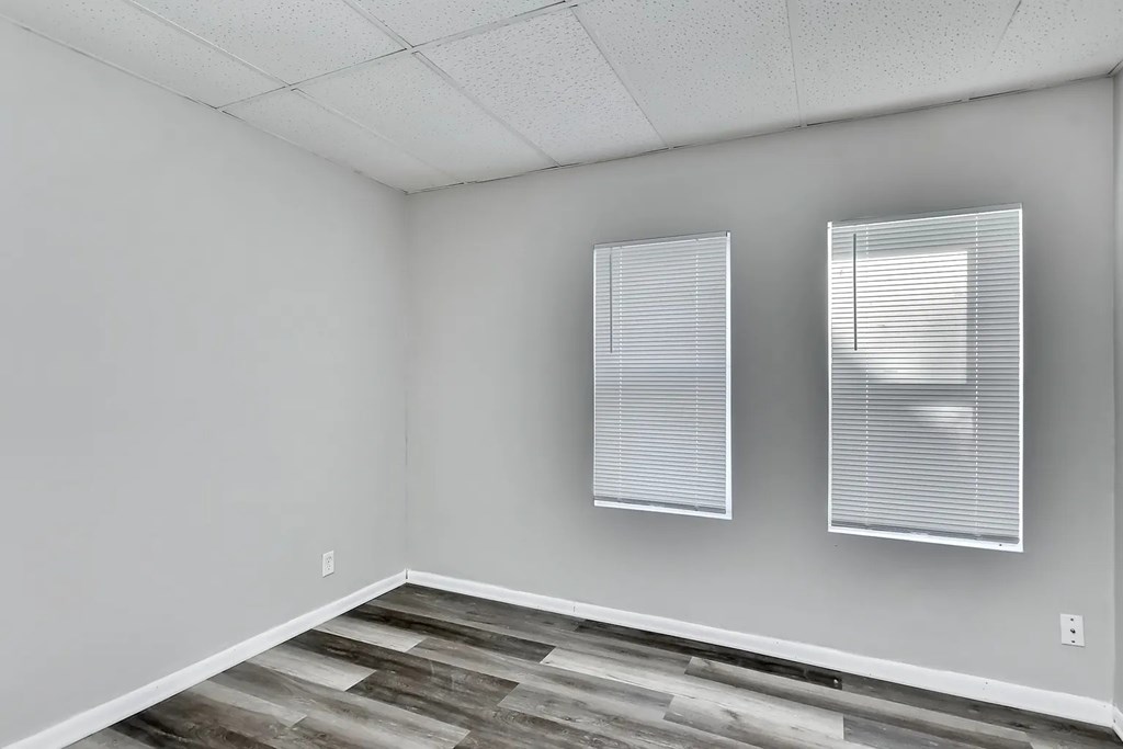 A room with a wooden floor and two windows with blinds.