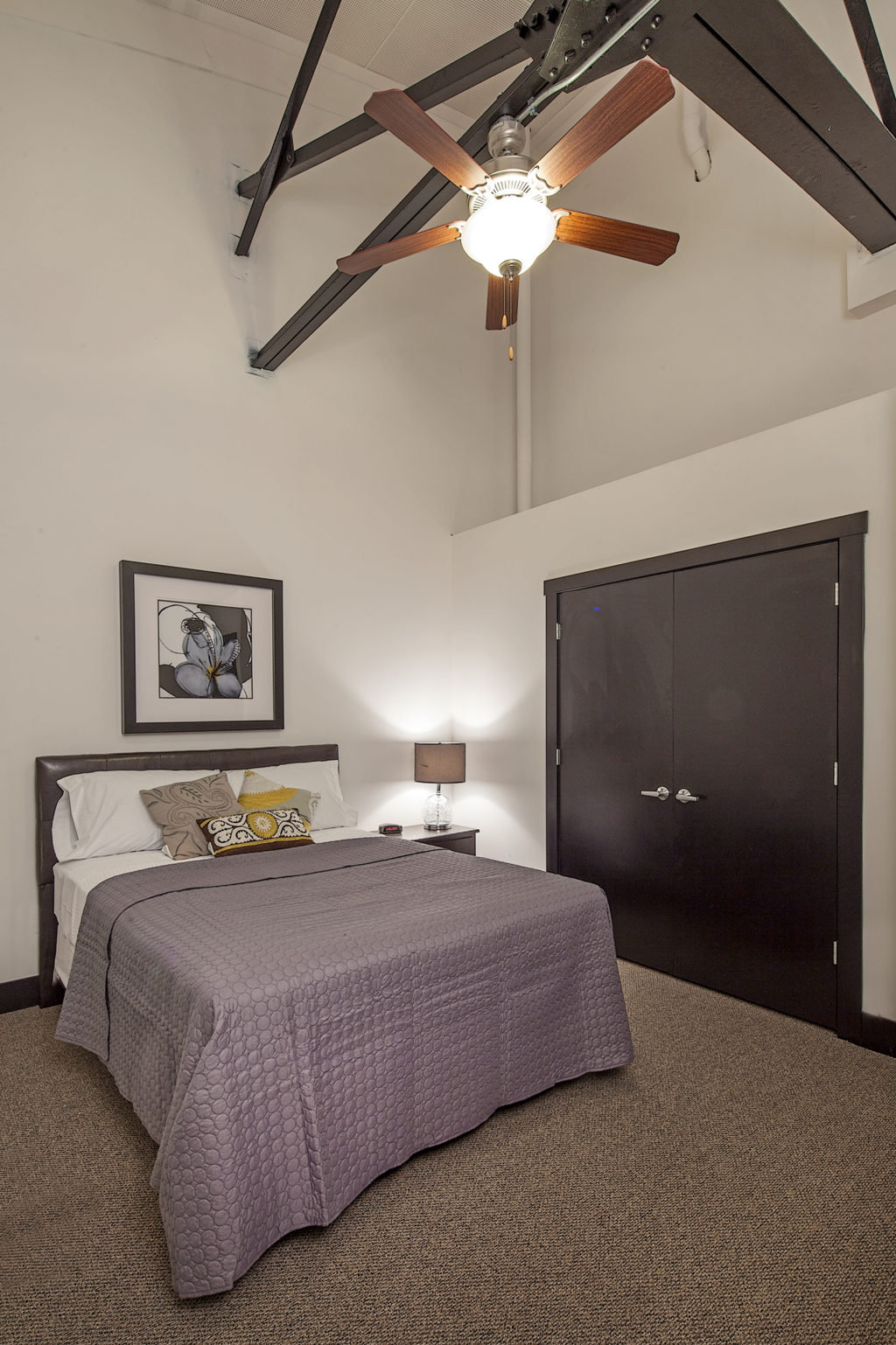 A bedroom with a bed, a ceiling fan, and a painting on the wall.