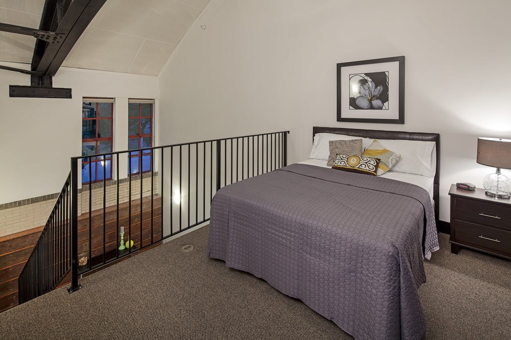 A bedroom with a bed, nightstand, and a picture on the wall.