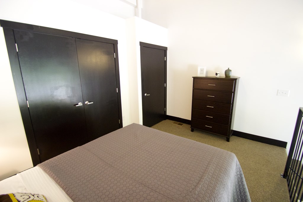 A bedroom with a bed, dresser, and two closets.