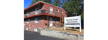Exterior view of a brick apartment building with balcony and Benson Crest Apartments signage.