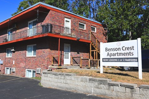 A red brick building with a sign that says Benson Crest Apartments.