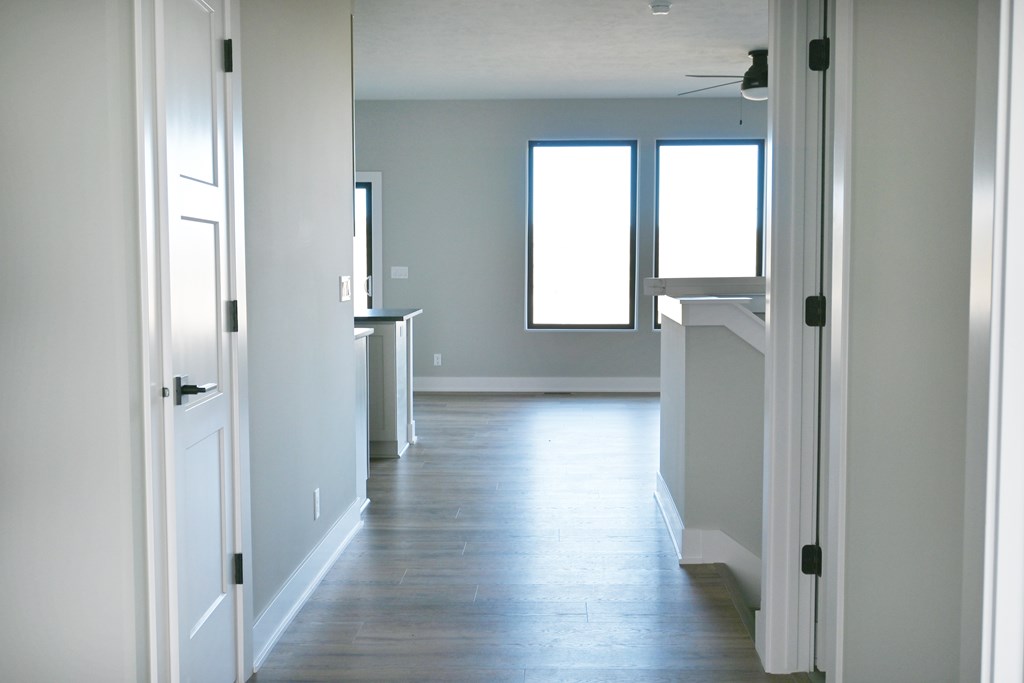 A long, narrow hallway with white doors on either side and a window with two panes of glass in the distance.