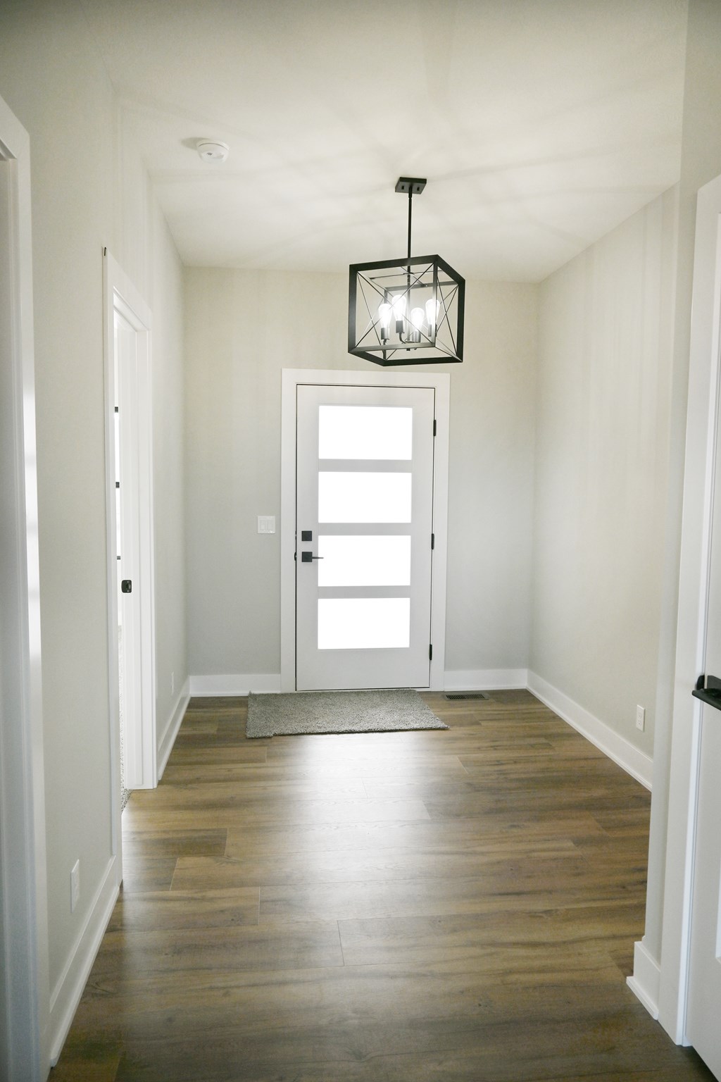 A hallway with a light hanging from the ceiling and a door at the end.