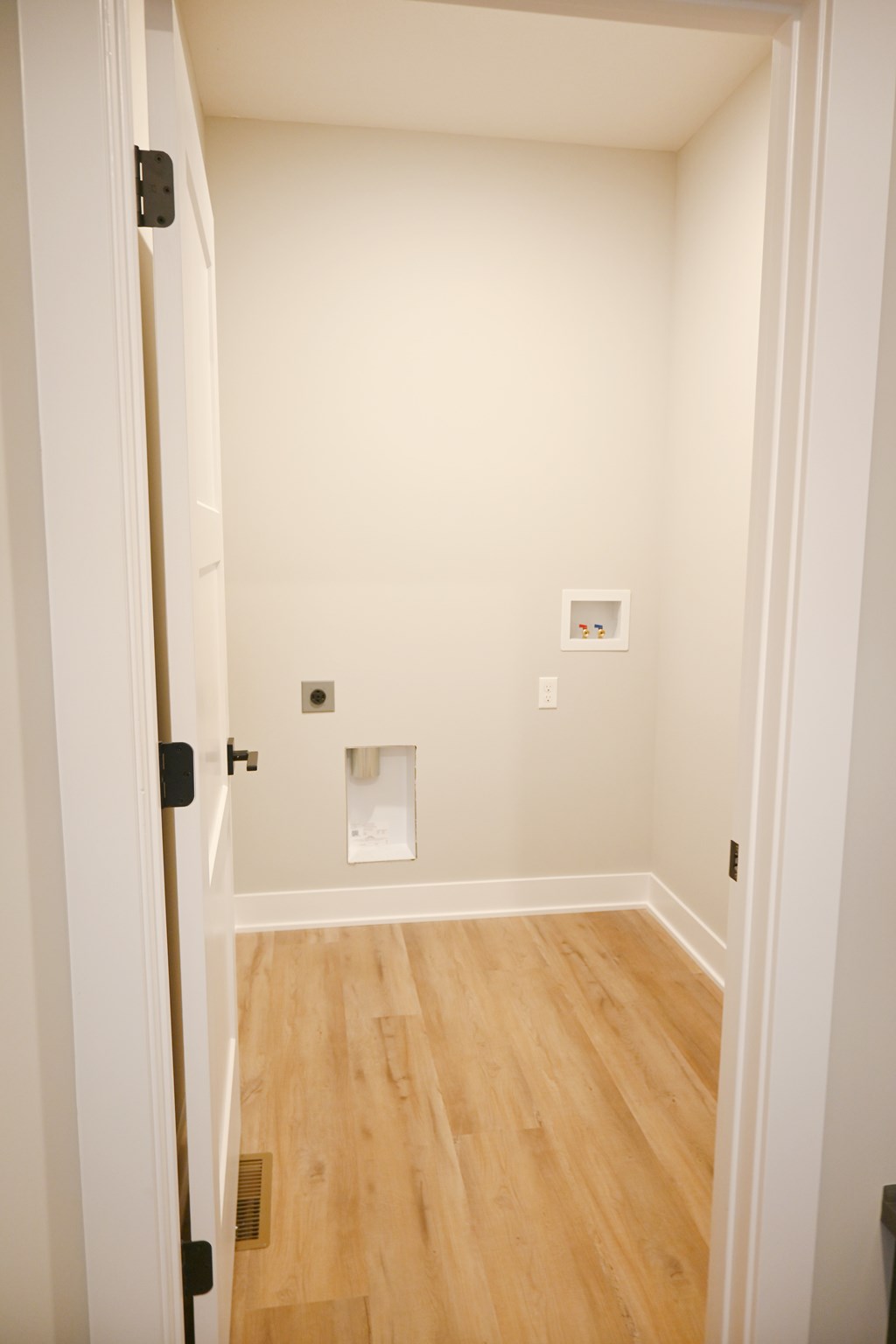 A white door is open to a room with wood flooring.