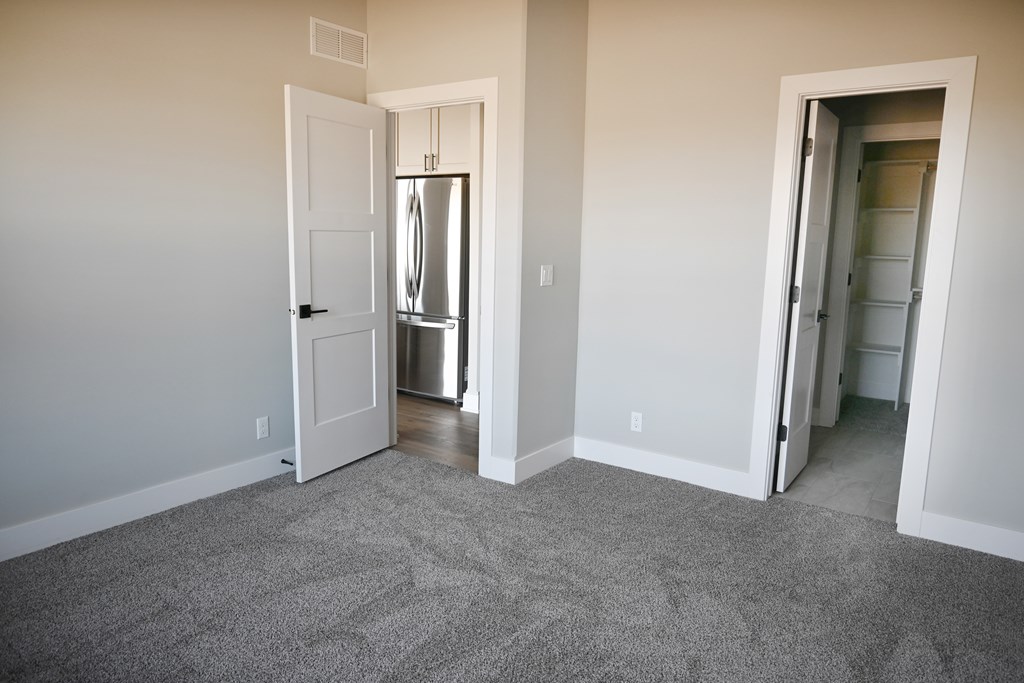 A room with a carpeted floor and a white door leading to a kitchen.
