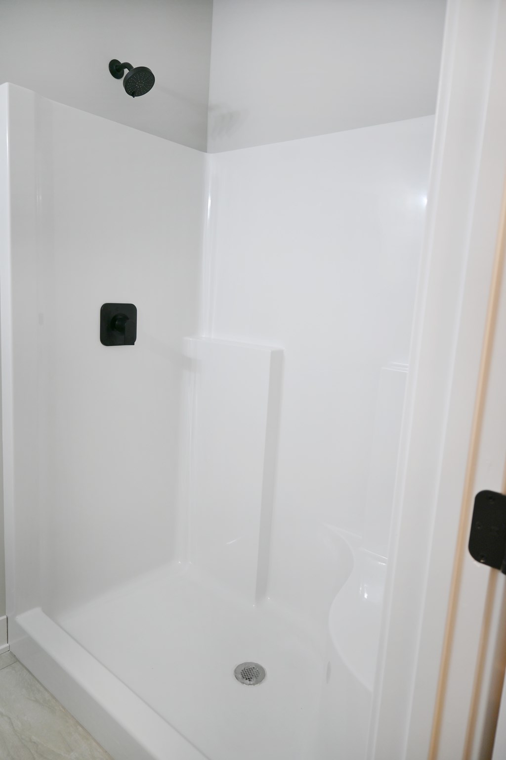 A white shower stall with a drain in the middle.