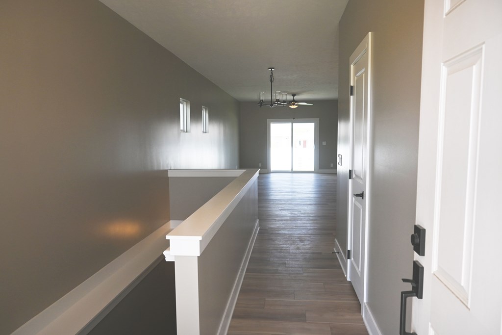 A long hallway with a white railing on the left side and a door on the right.