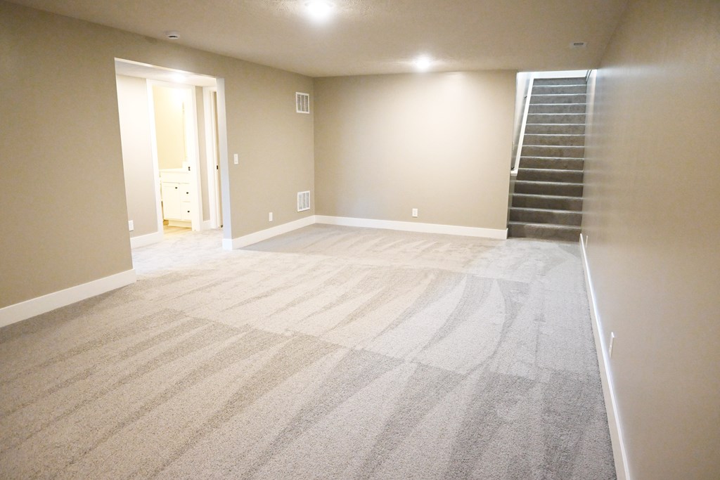 A room with a carpeted floor and a staircase on the right side.