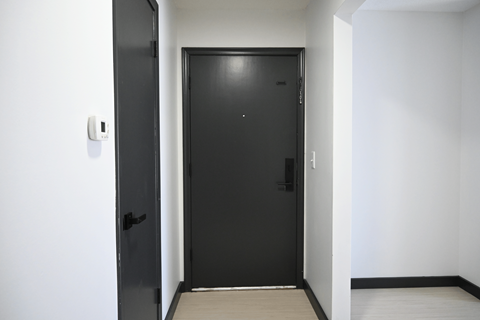 A black door with a handle and a lock is in a white room.