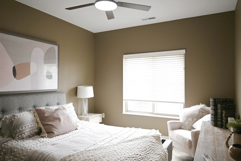 A bedroom with a large bed, a white chair, and a painting on the wall.
