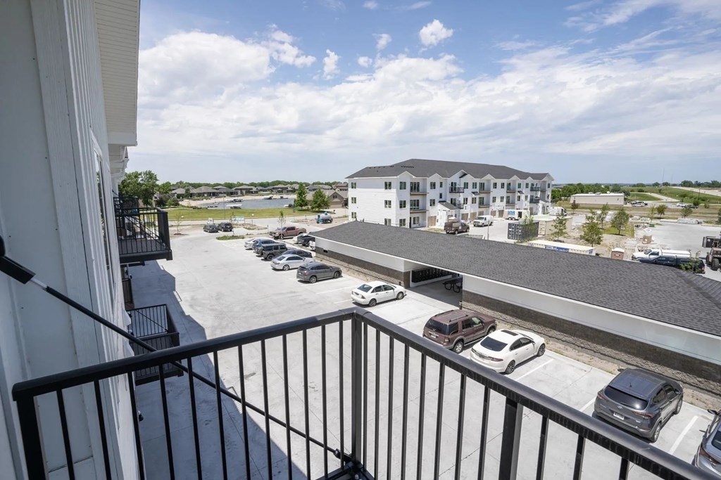 A balcony view of a parking lot with cars and a building in the distance.