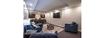 Living area with sofa, accent chairs, coffee table, wall mounted television and carpet flooring at Heartland Flats Alliance.