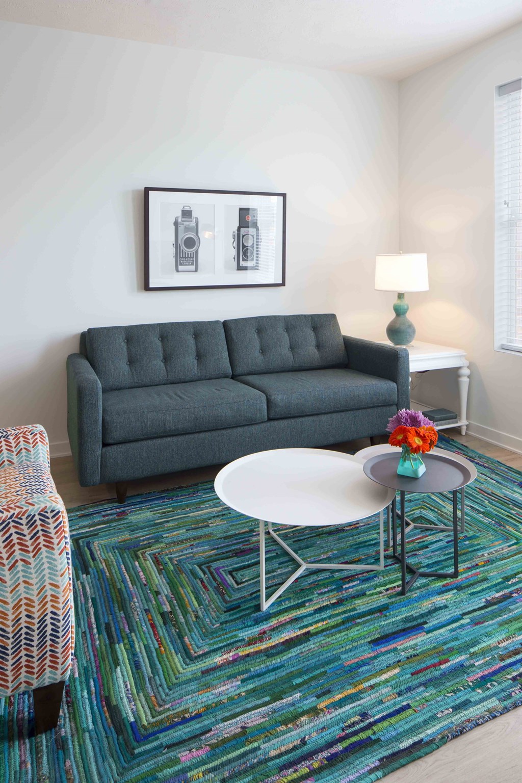 A grey sofa with a white table in front of it and a colorful rug on the floor.