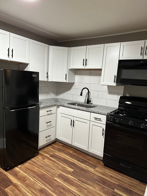 A black refrigerator stands in a kitchen with white cabinets.