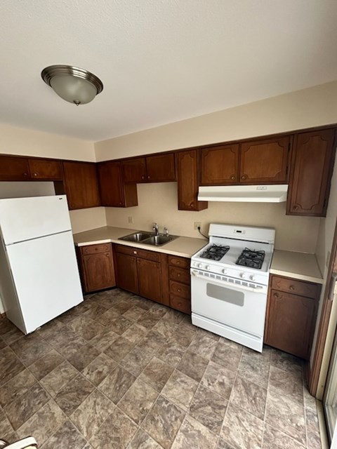 A kitchen with a white fridge, white stove, and brown cabinets.