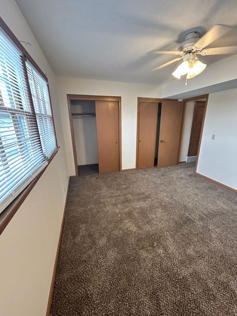A room with a carpeted floor, a ceiling fan, and three doors.