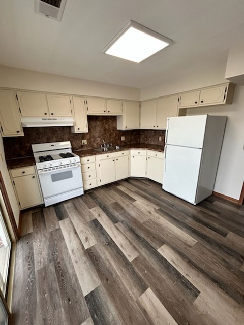 A kitchen with a white fridge and wooden floors.