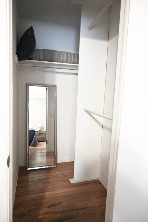 A mirror on the wall reflects a bedroom with a bed and a dresser.