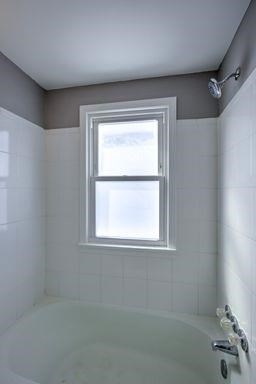A small window in a tiled bathroom with a tub.