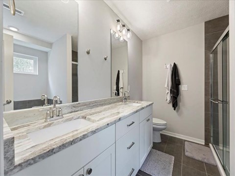 A bathroom with a marble countertop and white cabinets.